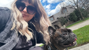 Olivia, a dog walker from Hands N Paws, smiles while walking a happy dog on a leash in a Columbus park, demonstrating her commitment to excellent pet care.